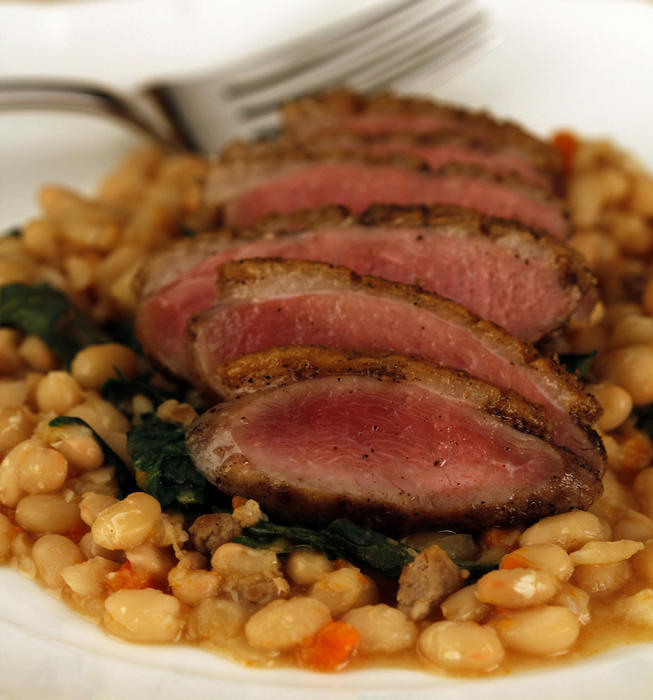 Crisp-skinned duck breasts on white beans with dandelion greens